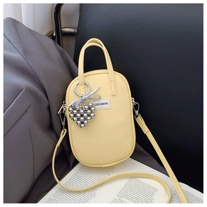 Detail of light yellow mini crossbody bag with silver heart charm and textile label