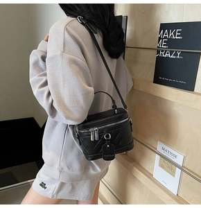 Detail of a black quilted cylindrical box bag worn crossbody by a model in a modern room