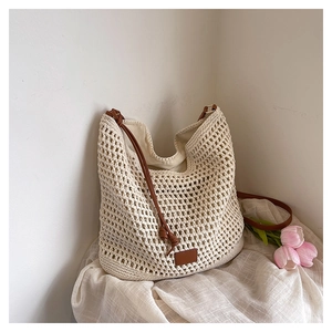 Detail of hollow-out beige crochet hobo bag with brown leather strap and decorative label