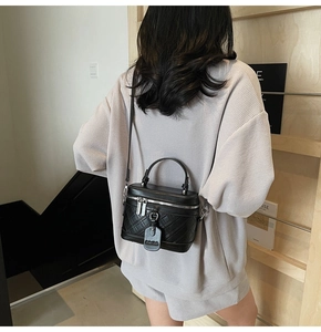 Detail of black quilted box bag shown on model in a minimalist modern interior