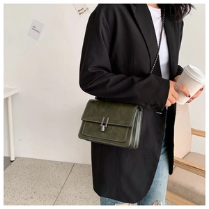 Detail of a dark green square crossbody bag with silver buckle worn with a black blazer
