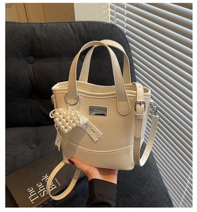 Detail of beige bucket bag with pearl heart charm and lace bow on textured sofa