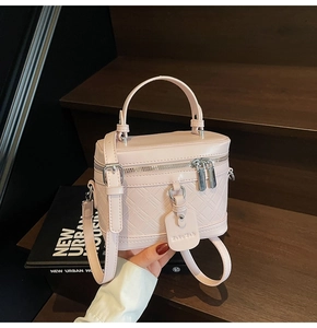 Pink quilted box bag with top handle and shoulder strap held against wooden stairs