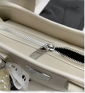 Detail of smooth silver zipper and pearl charm on a beige leather bucket bag