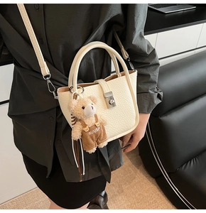 Detail of off-white lychee grain leather bucket bag with silver buckle and bear charm