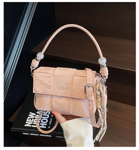 Detail of pink woven crossbody bag with pearl charms and logo on dark wooden background