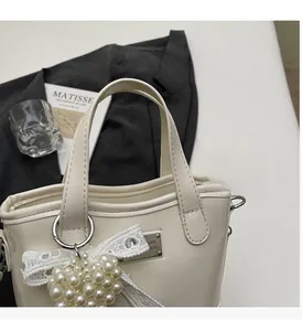 Detail of cream glossy bucket bag featuring pearl heart charm and lace bow decoration