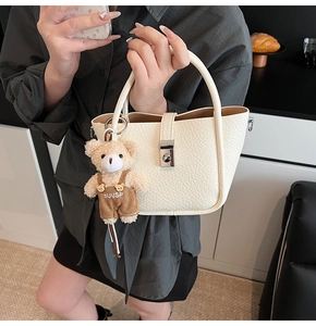 Detailed macro of cream lychee texture handbag with metal buckle and plush bear charm