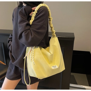 Detail of light yellow tote bag featuring scrunchie shoulder strap and woven tassels