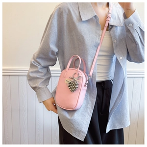 Pink faux leather phone bag detail featuring a metallic grape charm and crossbody strap