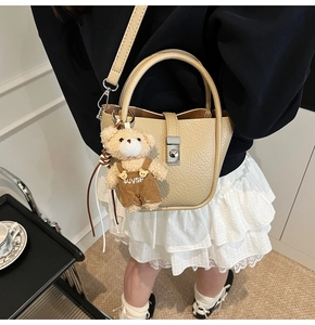 Detail of beige bucket bag with lychee texture leather and a cute bear plush pendant