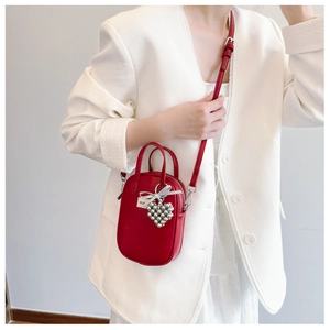 Detail of red crossbody phone bag with heart charm on a model in white blazer