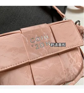 Close-up of pink woven leather shoulder bag showing the metal logo and textured grid finish