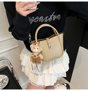 Detailed view of beige lychee leather bucket bag with metal lock and teddy bear charm