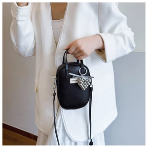 Close-up of a black crossbody phone bag with dual handles and silver bead charms on a model