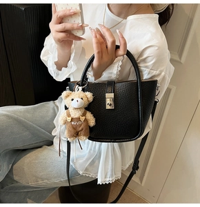 Detail of black pebbled leather bucket bag with metal clasp and plush bear charm