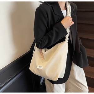 Detail of minimalist cream tote bag showing ruched strap and stylish brand label detail