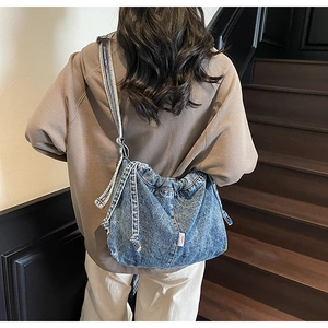Détail du sac bandoulière en denim bleu délavé avec design à cordon et étiquette latérale