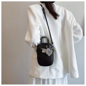 Detail of minimalist black crossbody phone bag with heart pearl charm on white suit