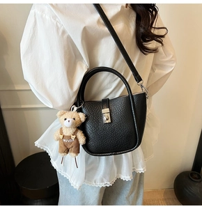 Close-up of black lychee grain leather bucket bag with silver lock and cute bear charm