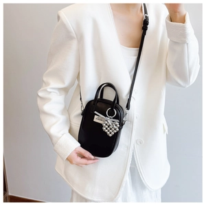 Detailed view of a black mini crossbody bag with heart bead charm on a white suit outfit