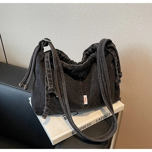 Détail du sac cabas en denim noir avec cordon et étiquette de marque sur un livre