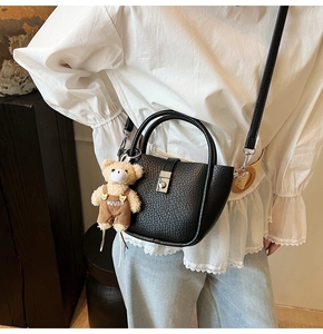 Detail of black pebbled leather bucket bag with silver metal clasp and plush bear charm