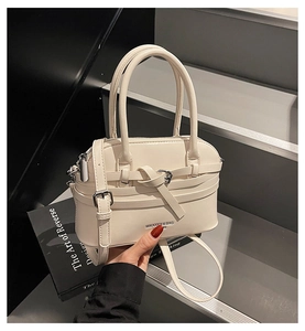 Detail of cream Boston bag with knot decorative strap and silver buckle on stone background