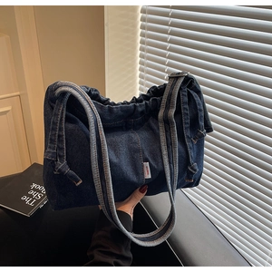 Détail du sac cabas en jean bleu foncé avec fermeture à cordon et texture plissée