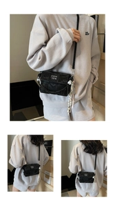 Detail of black woven texture crossbody bag with white lettering and tassel charm