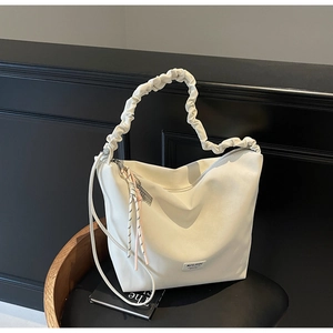 Detail of soft cream white tote bag featuring pleated handle and braided cord charm