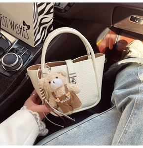 Detailed macro view of white pebble leather bucket bag with a cute teddy bear charm