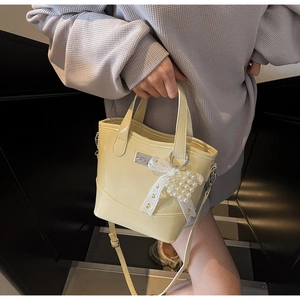 Detail of creamy yellow patent leather bucket bag with lace bow and pearl charm