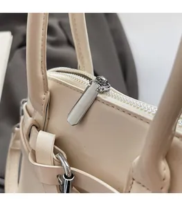 Close-up of silver metal zipper pull and fine stitching on beige shell handbag