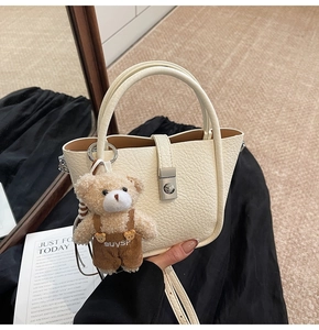 Detail of off-white bucket bag with lychee texture and cute teddy bear charm