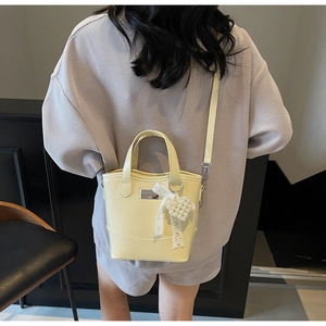 Detail of cream yellow bucket bag with lace bow and pearl heart charm on a model