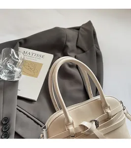 Close-up of cream leather handbag with rounded handle and metallic buckle detail