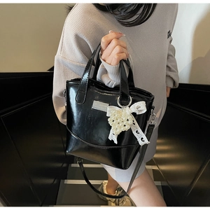 Detail of glossy black bucket bag featuring a pearl heart charm and lace bow accessory
