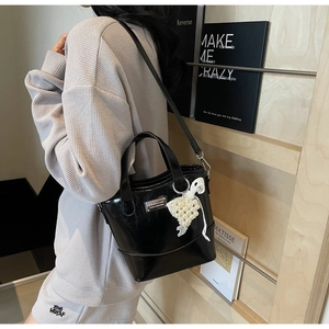 Detail of black patent leather bucket bag with pearl grape charm and elegant metal logo plate