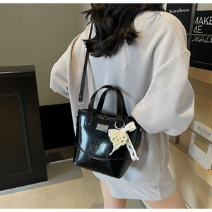 Polished black bucket bag with pearl bow charm and shoulder strap shown in a model shot