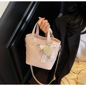 Detail of pink faux leather bucket bag with pearl heart charm and white lace bow