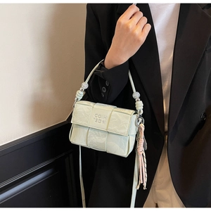 Detail of mint green woven crossbody bag featuring beaded handle and decorative tassel