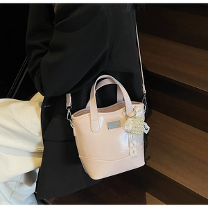 Detail of pink glossy bucket bag with pearl lace charm worn by model on stairs