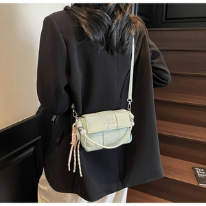 Detail of mint green woven crossbody bag featuring pearl handle and side fringe tassel