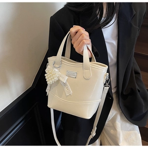 Detail of off-white bucket bag featuring a pearl heart charm and lace bow decoration