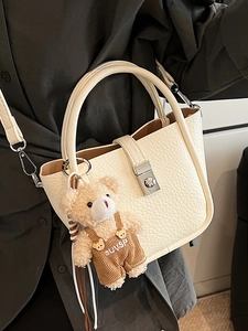 Minimalist white bucket bag with pebble leather texture and a cute teddy bear pendant