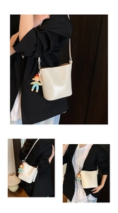 Detail of creamy white bucket bag with glossy patent texture and colorful clown charm