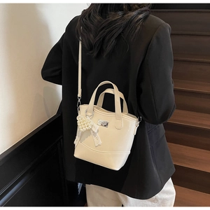 Close-up of cream bucket bag with pearl heart charm and lace bow on a black blazer