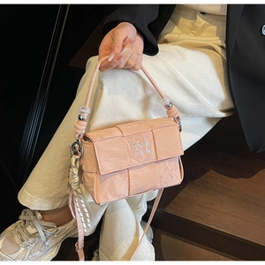 Detail of light pink woven square handbag with beaded strap on a dark wooden background