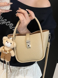 Minimalist beige pebble leather bucket bag with silver buckle and plush bear pendant